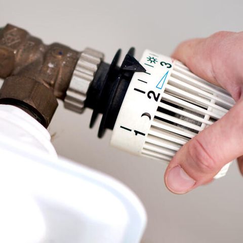 Eine Frau dreht am Thermostat einer Heizung
