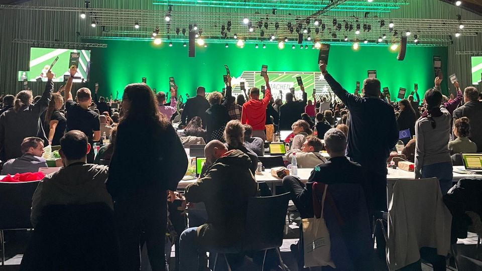 View from behind of people in front of a green background in a hall, each holding up a card. View from behind of people in front of a green background in a hall, each holding up a card.