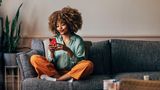 Eine Frau sitzt auf einem Sofa mit dem Handy in der Hand
