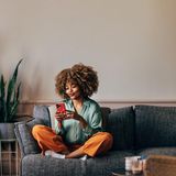 Eine Frau sitzt auf einem Sofa mit dem Handy in der Hand