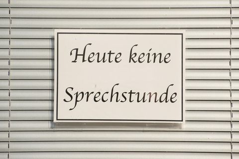 Ein Schild mit der Aufschrift "Heute keine Sprechstunde" hängt im Fenster einer Arztpraxis vor einer Jalousie