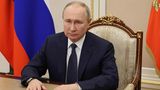 Wladimir Putin bei sitzt an einem Tisch vor einer Russland-Flagge