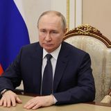 Wladimir Putin bei sitzt an einem Tisch vor einer Russland-Flagge