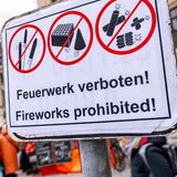 Ein Verbotsschild, dahinter gehen Menschen spazieren