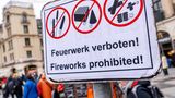 Ein Verbotsschild, dahinter gehen Menschen spazieren