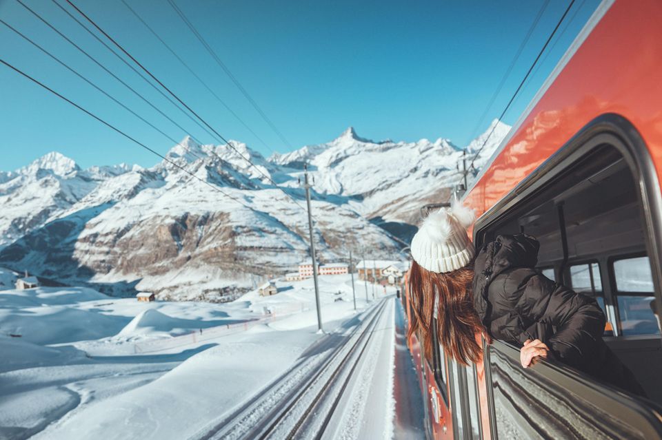 Reisetrends Eine Frau schaut aus dem Fenster eines Zuges in einer verschneiten Berglandschaft