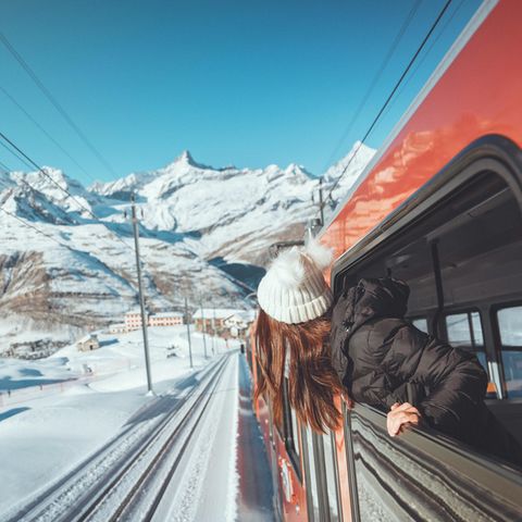 Eine Frau schaut aus dem Fenster eines Zuges in einer verschneiten Berglandschaft