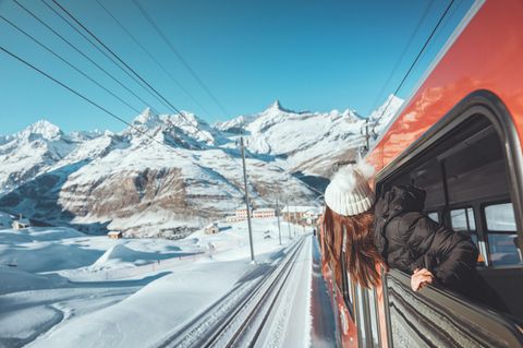 Eine Frau schaut aus dem Fenster eines Zuges in einer verschneiten Berglandschaft