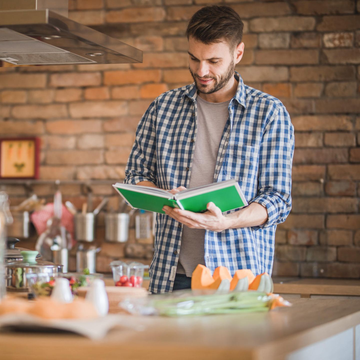 Lächelnder Mann mit Kochbuch für die Zubereitung von Speisen in der Küche.