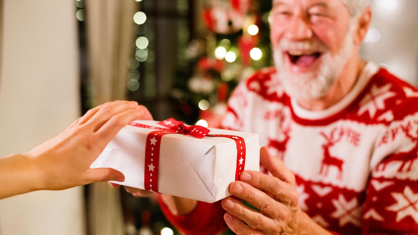 Älterer Mann vor Weihnachtsbaum hält ein Geschenk