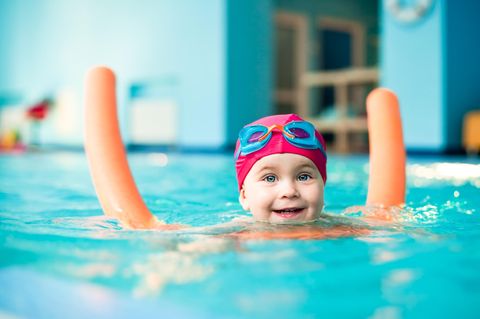 Schwimmhilfen für Kinder: Kleines Mädchen mit orangener Poolnudel im Wasser