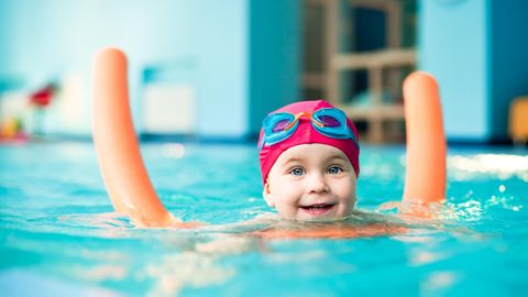 Schwimmhilfen für Kinder: Kleines Mädchen mit orangener Poolnudel im Wasser