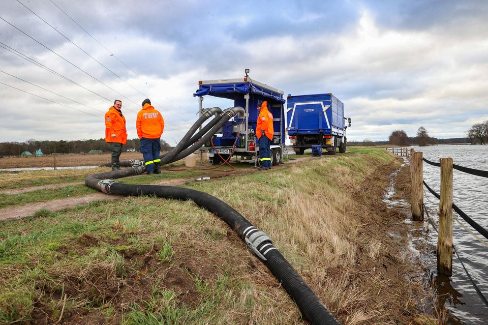Drei Helfer des THW pumpen Wasser aus einem überschwemmten Bachlauf