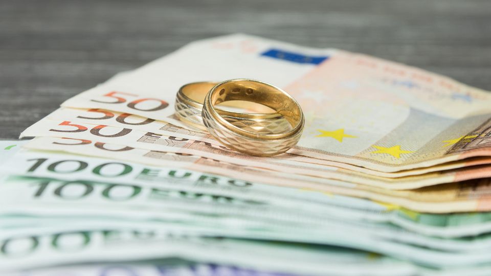 Scheidung: Zwei Eheringe liegen auf 50-Euro und 100-Euro Scheinen