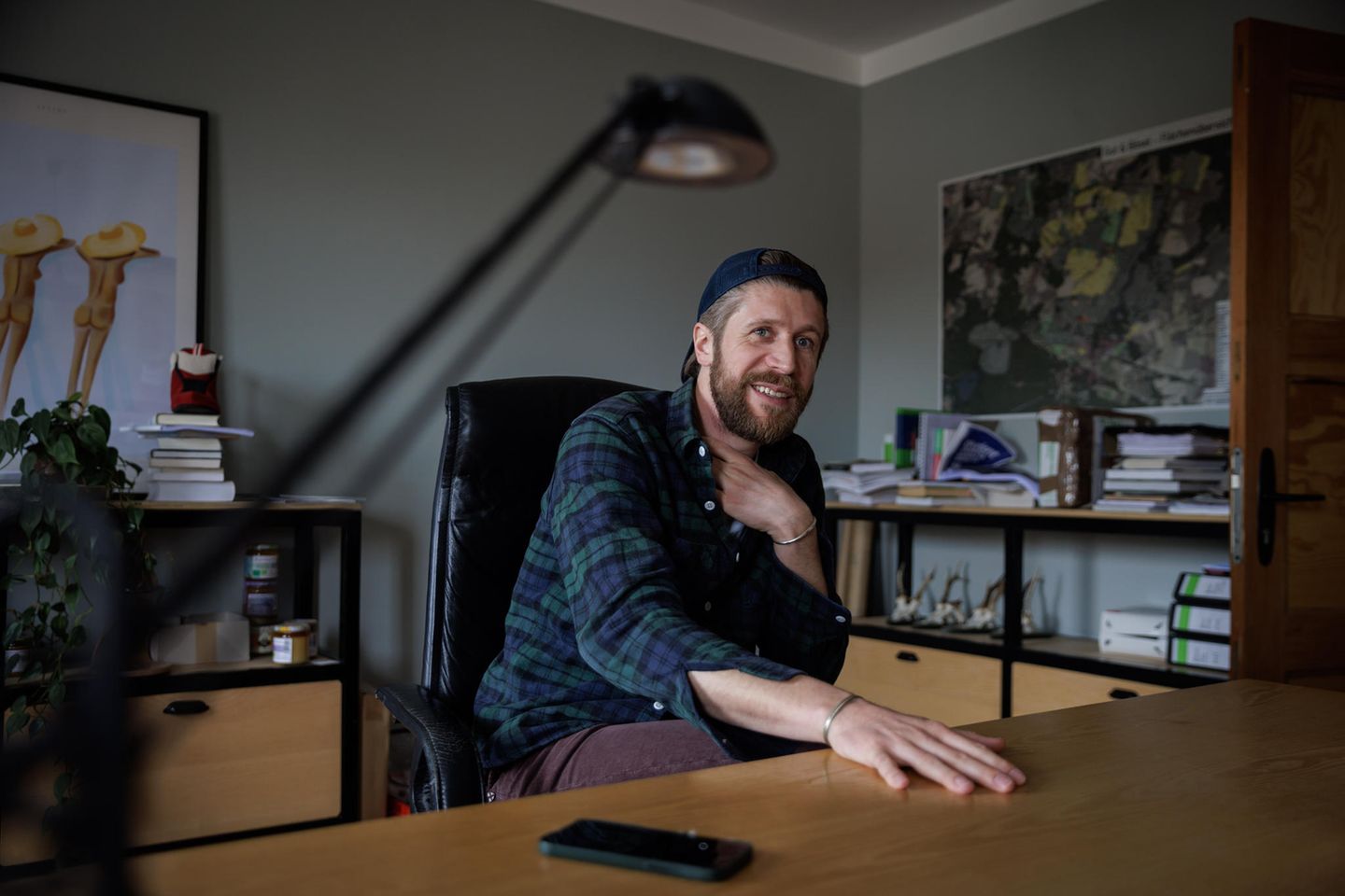 Mann mit kariertem Hemd und Basecap sitzt im Büro