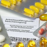 Medikamentenblister liegen auf einer Arbeitsunfähigkeitsbescheinigung