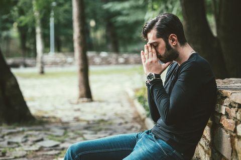 Ein Mann sitzt allein auf einer Bank im Wald