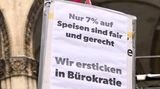 Auf einem Schild fordern Protestierende 7 statt 19 Prozent Mehrwertsteuer