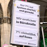 Auf einem Schild fordern Protestierende 7 statt 19 Prozent Mehrwertsteuer