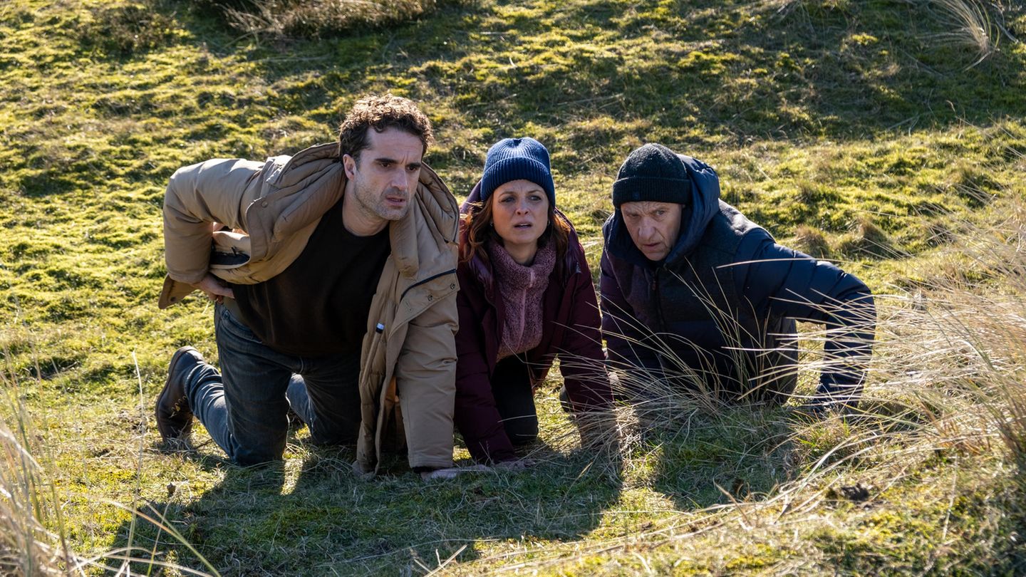 Carl Sievers (Peter Heinrich Brix, r.), Hinnerk Feldmann (Oliver Wnuk) und Ina Behrendsen (Julia Brendler) suchen Schutz hinter einem Hügel in einer Szene des Films "Nord Nord Mord - Sievers und die fünf Fragezeichen"