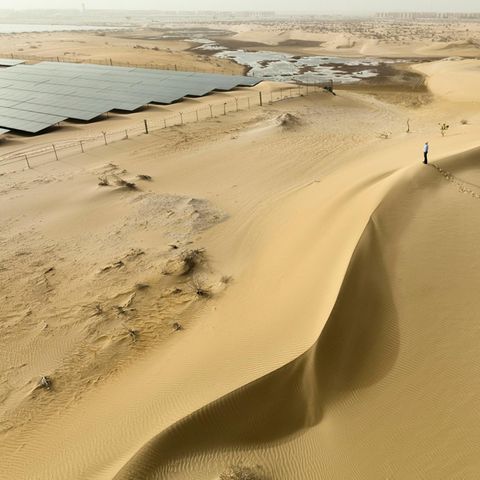 Ein Mann steht auf einer Düne und blickt auf Solaranlagen in der Wüste