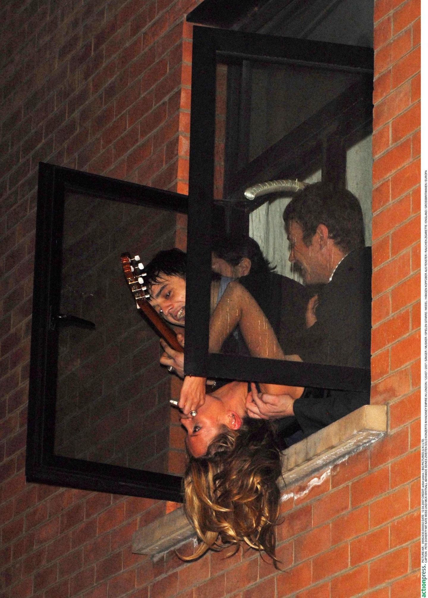 Pete Doherty, Kate Moss und Mick Whitnall in einem Fenster. Doherty hält eine Gitarre in der Hand