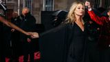 Kate Moss trägt ein schwarzes Kleid und die Hand einer Frau, die im Bild aber nicht zu sehen ist