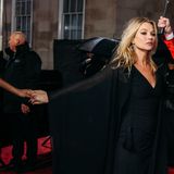 Kate Moss trägt ein schwarzes Kleid und die Hand einer Frau, die im Bild aber nicht zu sehen ist