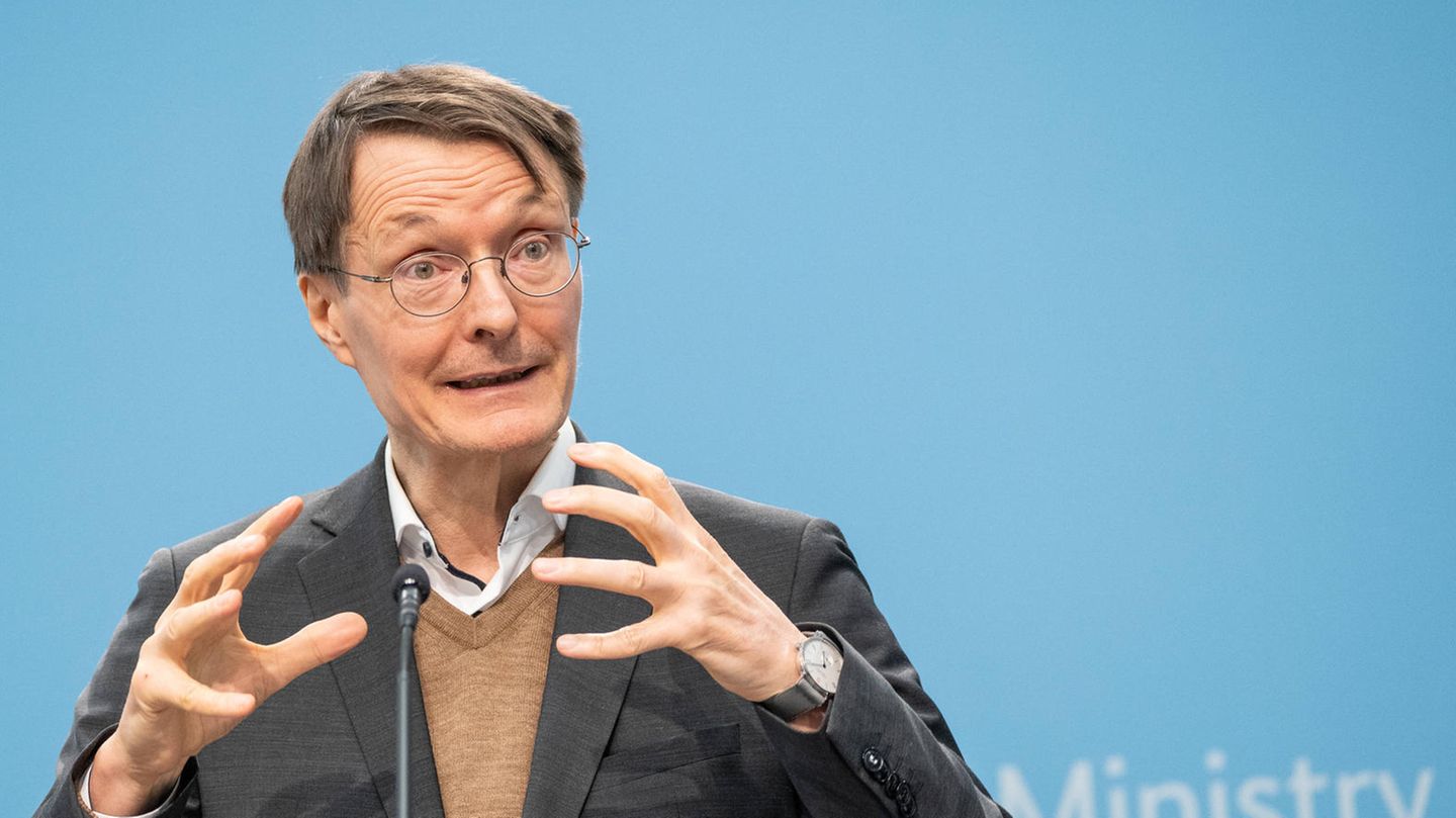 Minister Karl Lauterbach bei der Pressekonferenz vor blauem Hintergrund.