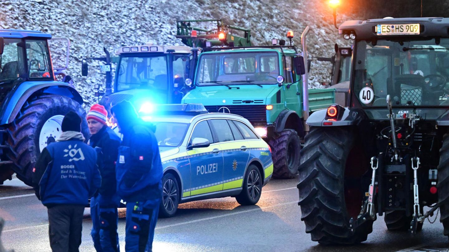 Ein Polizeiauto steht zwischen einer Gruppe Traktoren, die die Zufahrt zur Autobahn A8 blockieren