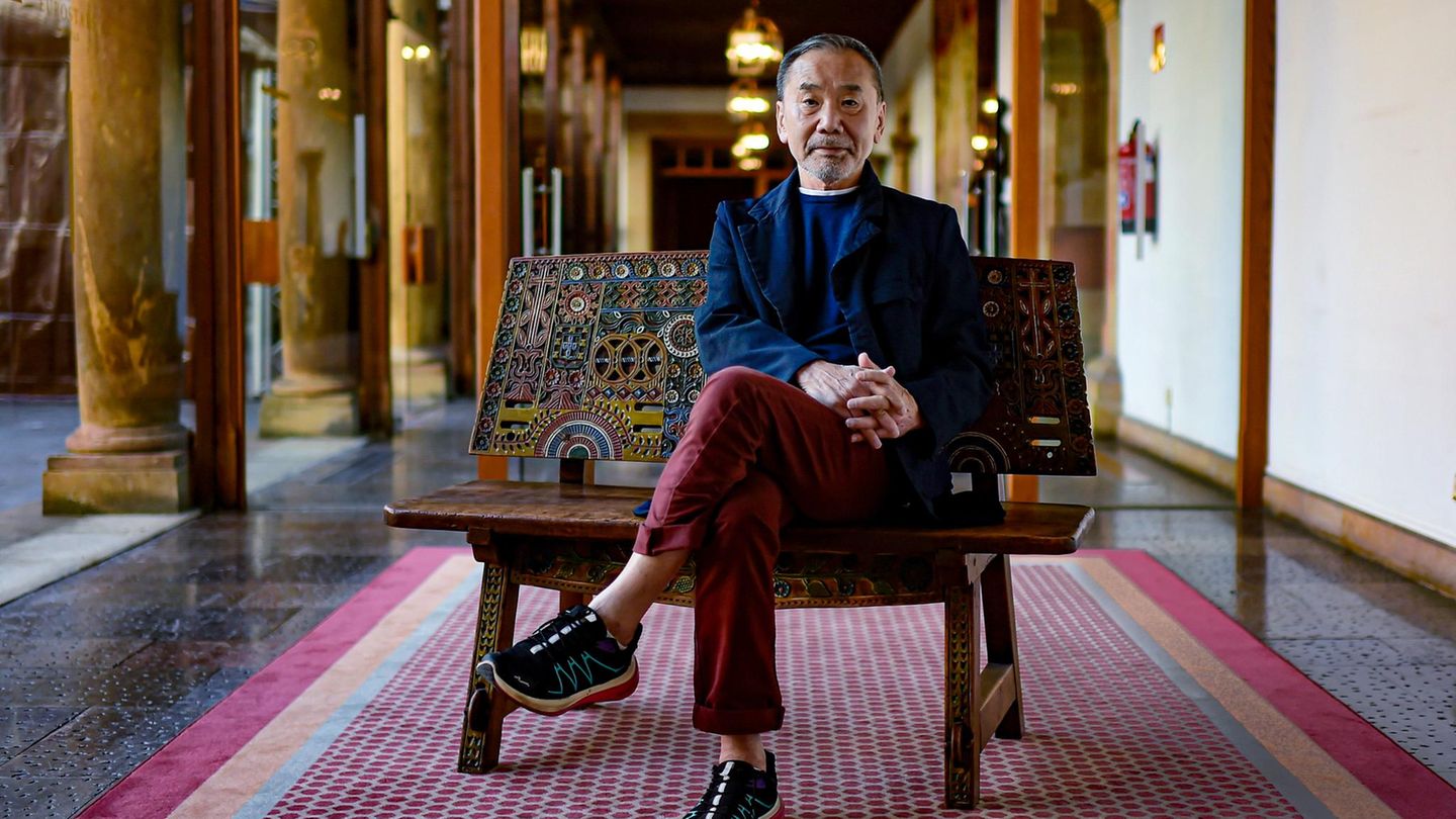 Japanischer Autor Haruki Murakami sitzt mit überkreuzten Beinen auf einer Bank.