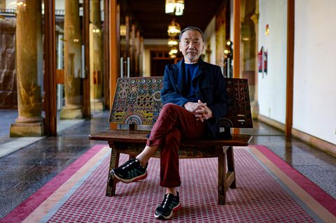 Japanischer Autor Haruki Murakami sitzt mit überkreuzten Beinen auf einer Bank.