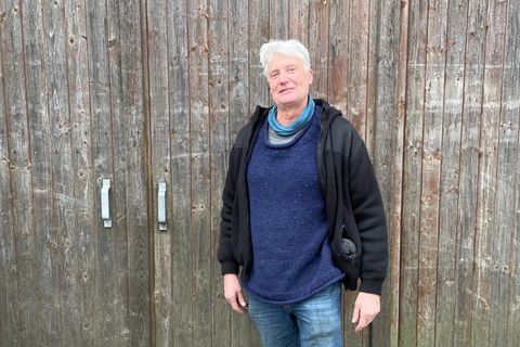 Ein Mann mit weißen Haaren und Fleecejacke steht vor einem Scheunentor.