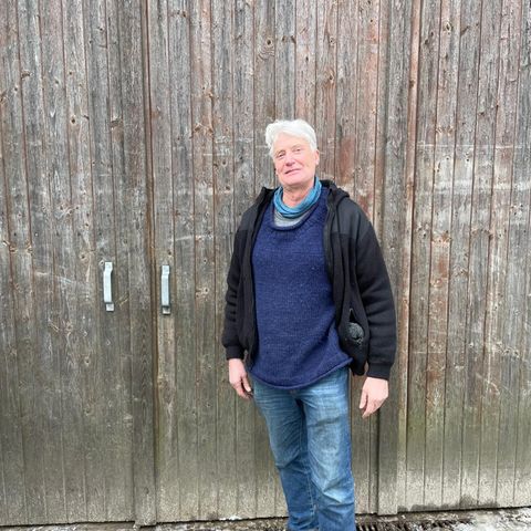 Ein Mann mit weißen Haaren und Fleecejacke steht vor einem Scheunentor.