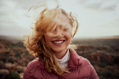 Stress reduzieren, das Gehirn entlasten: Die Haare einer Frau fliegen im Wind, sie lächelt mit geschlossenen Augen