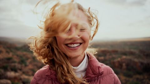 Stress reduzieren, das Gehirn entlasten: Die Haare einer Frau fliegen im Wind, sie lächelt mit geschlossenen Augen