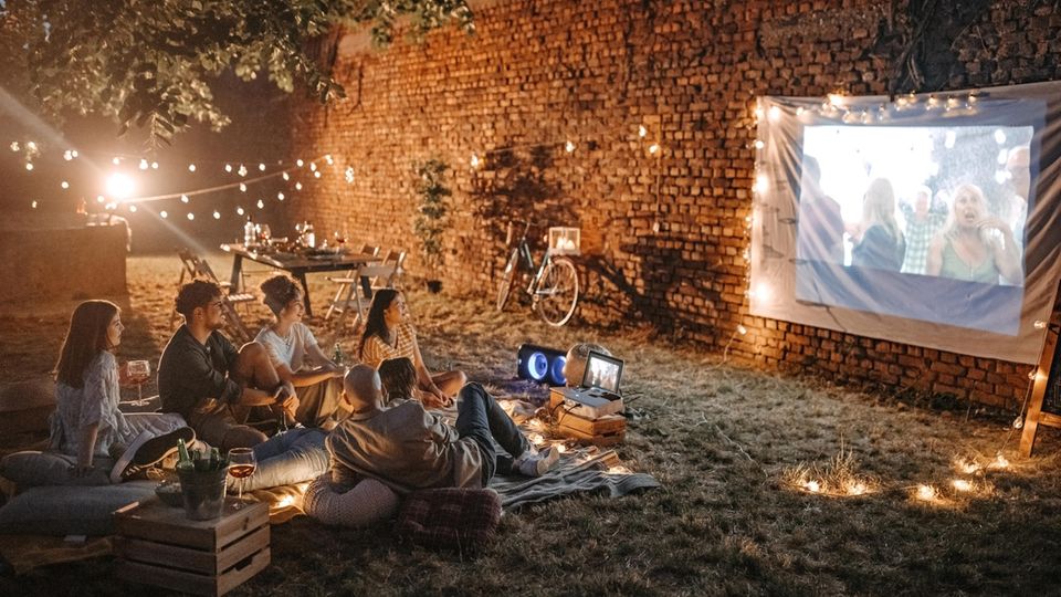 Beamer für draußen: Eine Gruppe junger Menschen schaut im Garten einen Film per Beamer