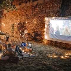 Beamer für draußen: Eine Gruppe junger Menschen schaut im Garten einen Film per Beamer