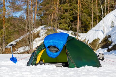 Schlafsack im Winter: Daunenschlafsack hängt zum Lüften über einem kleinen Zelt im Schnee