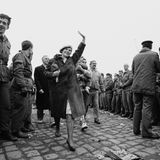 Menschen aus Ostberlin überqueren die Grenze, eine Frau hebt grüßend die Hand und lächelt