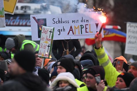 Ein Demonstrant hält eine bengalische Fackel in der Hand. Dahinter ein Schuld: Schluss mit dem Gehampel
