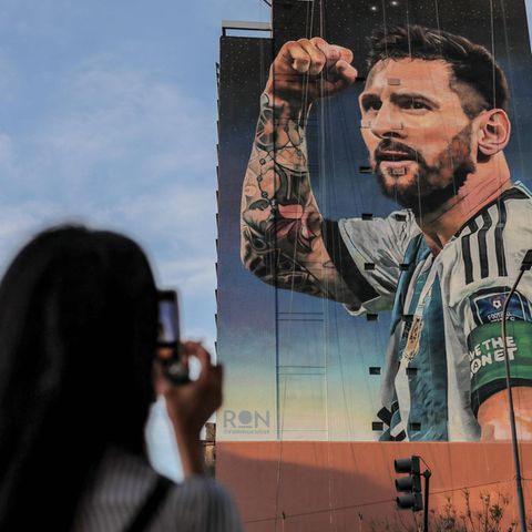 Lionel Messi als Bild auf einer Hauswand, eine Frau fotografiert ihn.