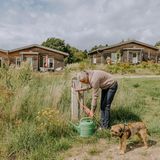 Ein Mann lässt Wasser in eine Gießkanne auf einer Wiese, neben ihm ein Hund