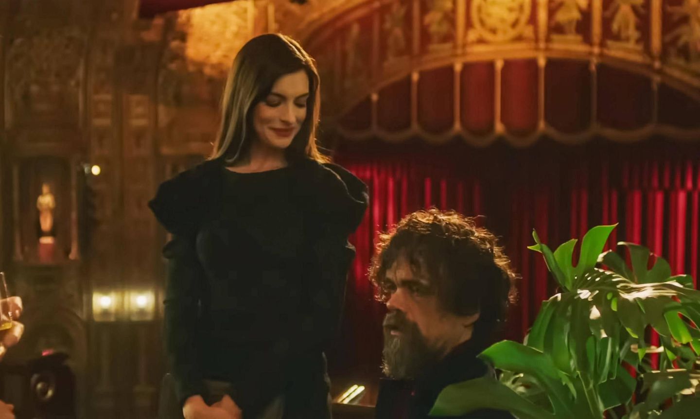 Anne Hathaway lächelt und steht neben Peter Dinklage, der ernst schaut