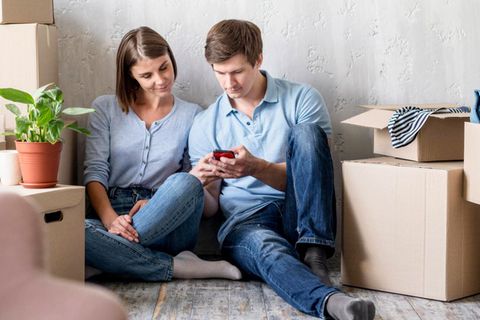 Umzug: Pärchen schaut beim Packen auf das Smartphone und zieht um