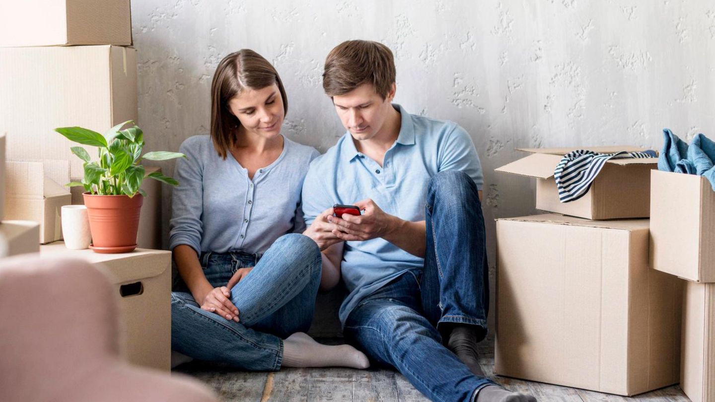 Umzug: Pärchen schaut beim Packen auf das Smartphone und zieht um