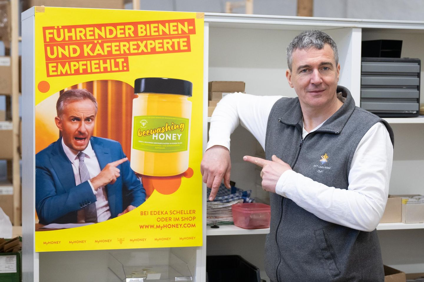 Böhmermann gegen Imker Ein Mann steht neben einem Plakat auf dem Jan Böhmermann Honig bewirbt
