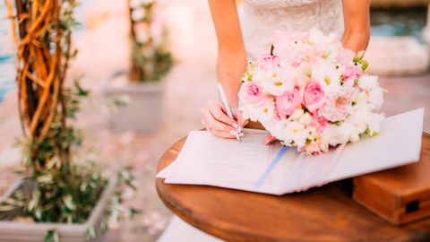 Eine Frau im Brautkleid unterschreibt den Ehevertrag und hält in der anderen Hand den Brautstraus
