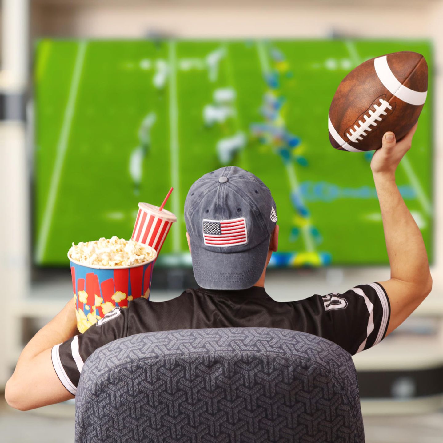 Super Bowl Gadgets: Footballfan sitzt mit Ball und Popcorn vor einem Fernseher