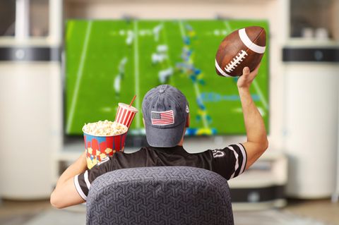 Super Bowl Gadgets: Footballfan sitzt mit Ball und Popcorn vor einem Fernseher